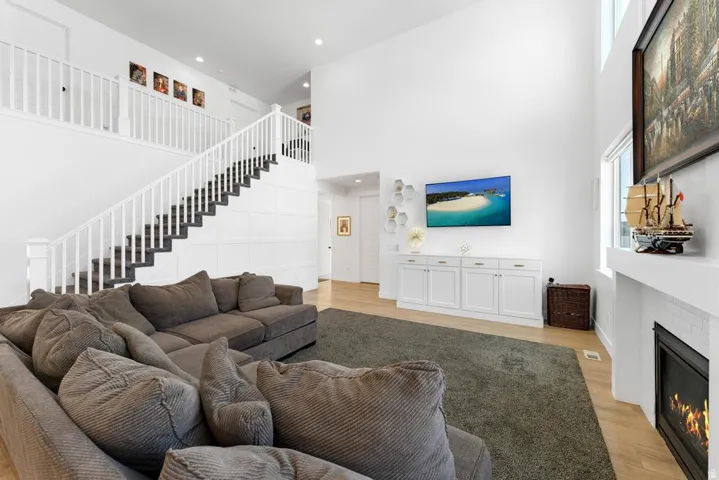 Two-story ceiling, light wood-finish flooring, built-in white cabinetry, white baluster staircase, and a fireplace with a white mantel and tile surround