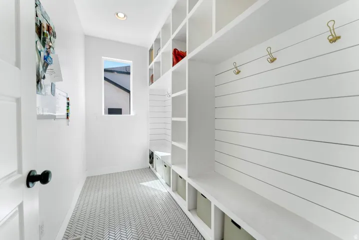 Built-in white storage cabinetry with open shelving and bench seating, complete with brass-finish hooks and a shiplap accent wall