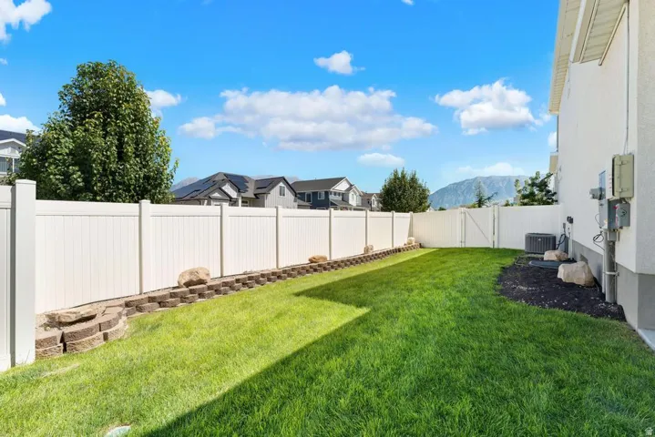 Expansive backyard with a manicured lawn, white privacy fencing, and a retaining wall