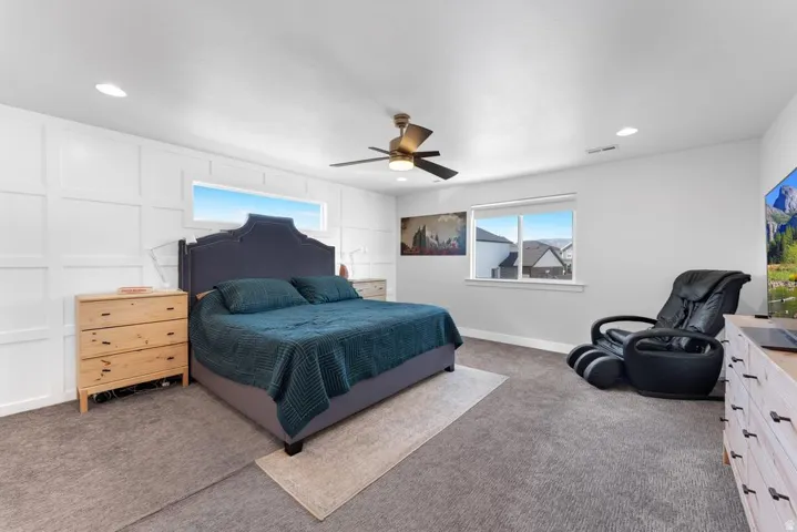 Textured accent wall, ceiling fan, recessed lighting, carpet flooring, multiple windows