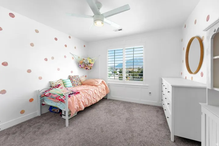 Window with plantation shutters, ceiling fan with integrated lighting, wall paneling, and wall-to-wall carpeting