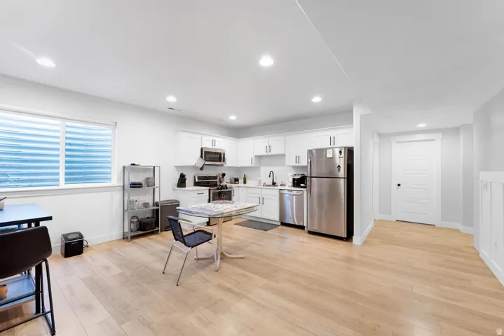 Open-concept living area featuring light wood-finish flooring, recessed lighting, and a kitchen with white cabinetry and stainless steel appliances