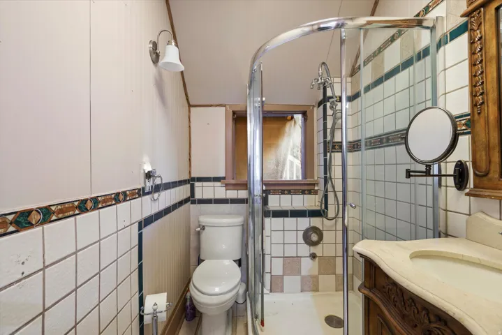 Curved glass shower enclosure, white tile surround with decorative trim, pedestal toilet, and wall-mounted vanity with integrated sink