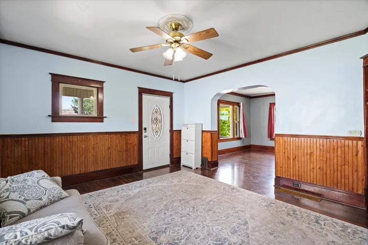 Wood-finish flooring, wood paneling, decorative window trim, arched doorway, and ceiling fan with light fixture