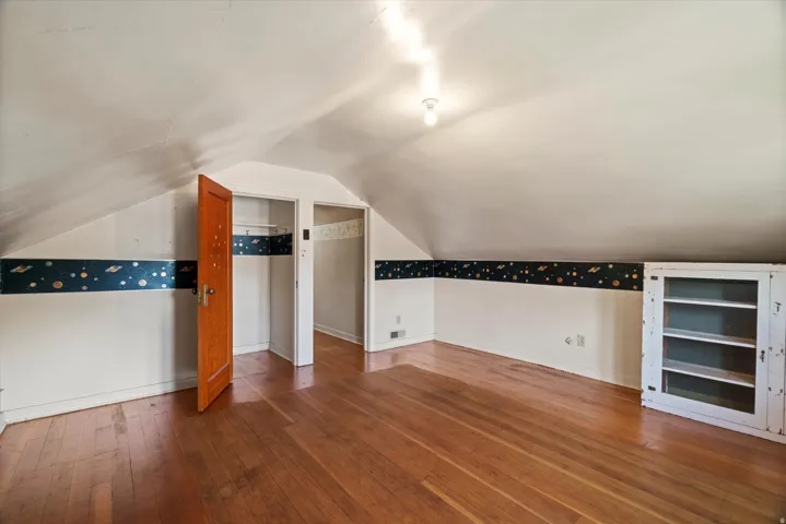 Sloped ceiling room featuring wood-finish flooring, two doorways, and a built-in shelving unit with glass panel doors