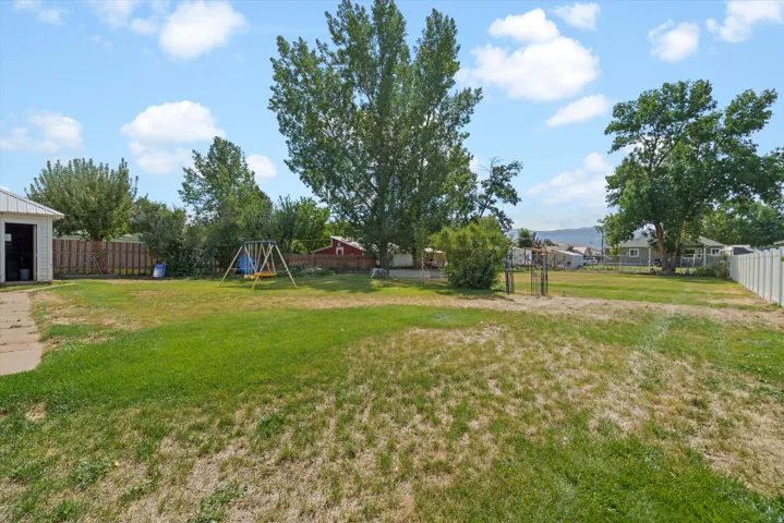 Expansive backyard with a manicured lawn, established trees, and perimeter fencing