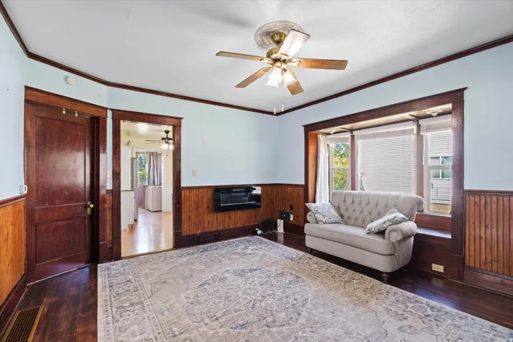 Hardwood flooring, wood paneling, wood window trim, bay window, and a ceiling fan with integrated lighting