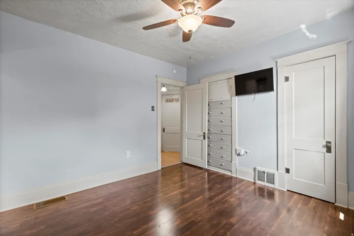 Wood-finish flooring, built-in storage with multiple drawers, and a ceiling fan with integrated lighting