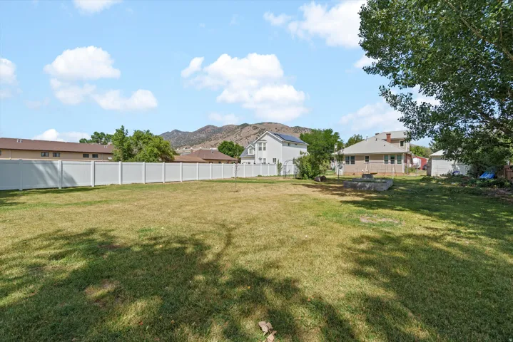 Expansive backyard featuring a white panel fence, mature trees, and mountainous scenery