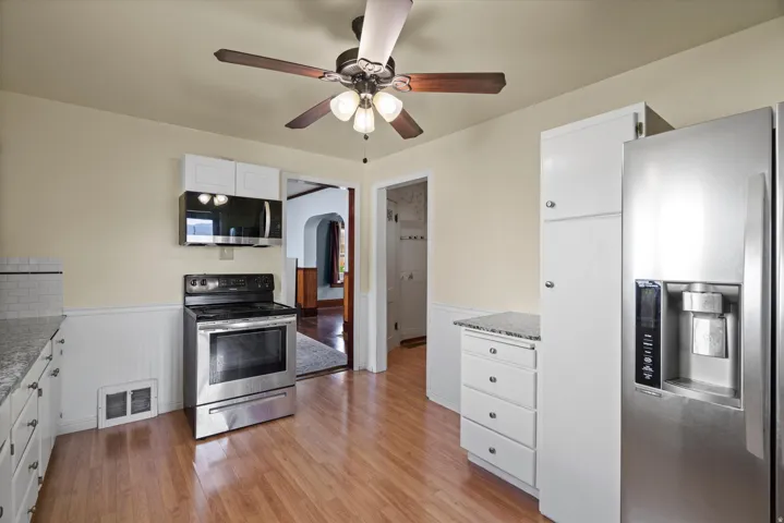 Kitchen featuring wood-finish flooring, white cabinetry, a subway tile backsplash, and stainless steel appliances