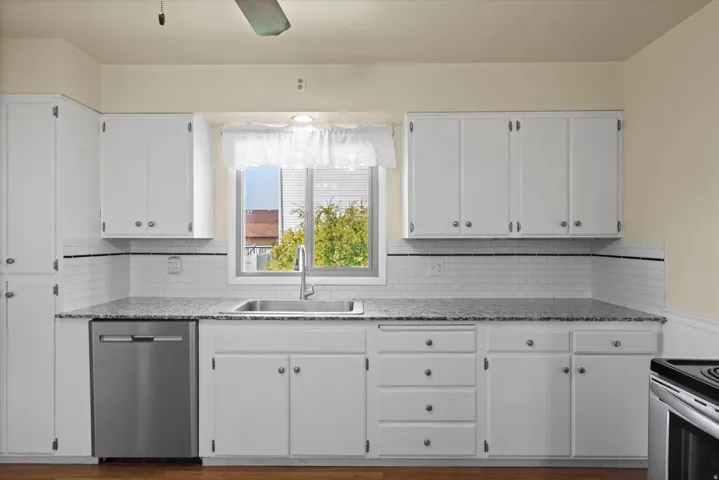 White cabinetry, wood-finish flooring, stainless steel dishwasher, undermount sink, and subway tile backsplash