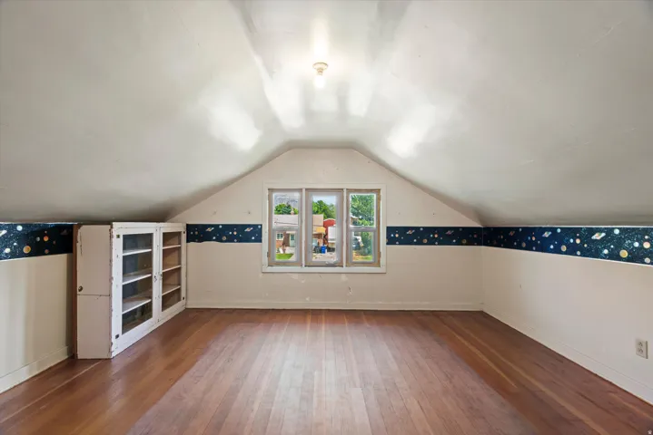 Bright attic room featuring vaulted ceilings with recessed lighting, hardwood flooring, and three triple-pane windows flooding the space with natural light