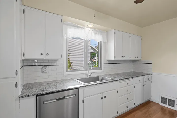 White shaker-style cabinetry with chrome hardware, subway tile backsplash with black accent tile, stainless steel undermount sink, wood-finish flooring, and light-toned countertops