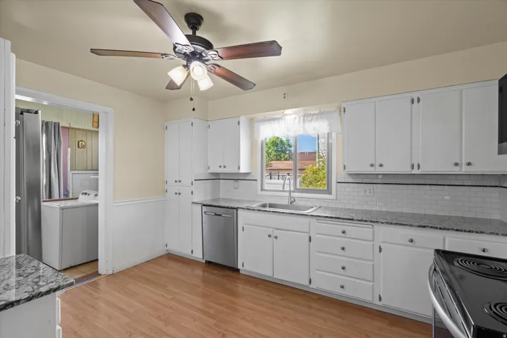 Kitchen featuring white cabinetry, light-toned wood-finish flooring, stainless steel dishwasher, a ceiling fan with integrated lighting, and a window with natural light