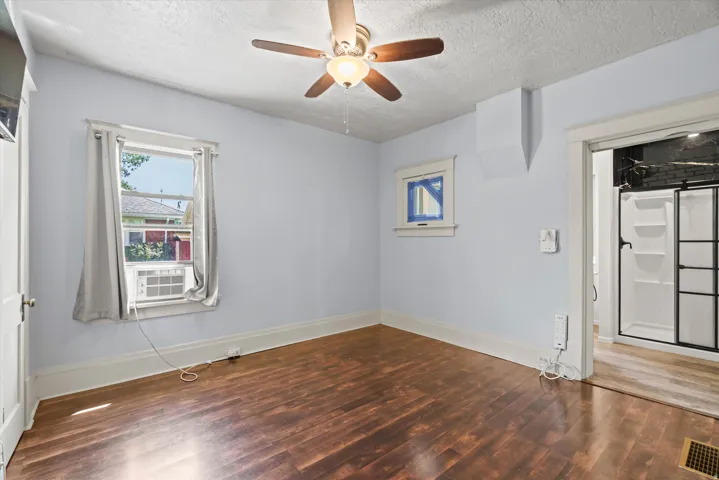 Wood-finish flooring, ceiling fan with integrated lighting, and a window with an air conditioning unit