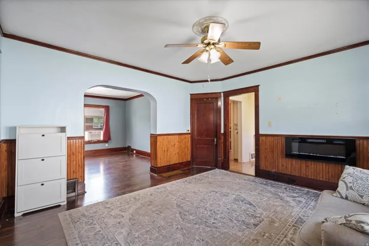 Hardwood-finish flooring, wood paneling, ceiling fan, and an arched doorway
