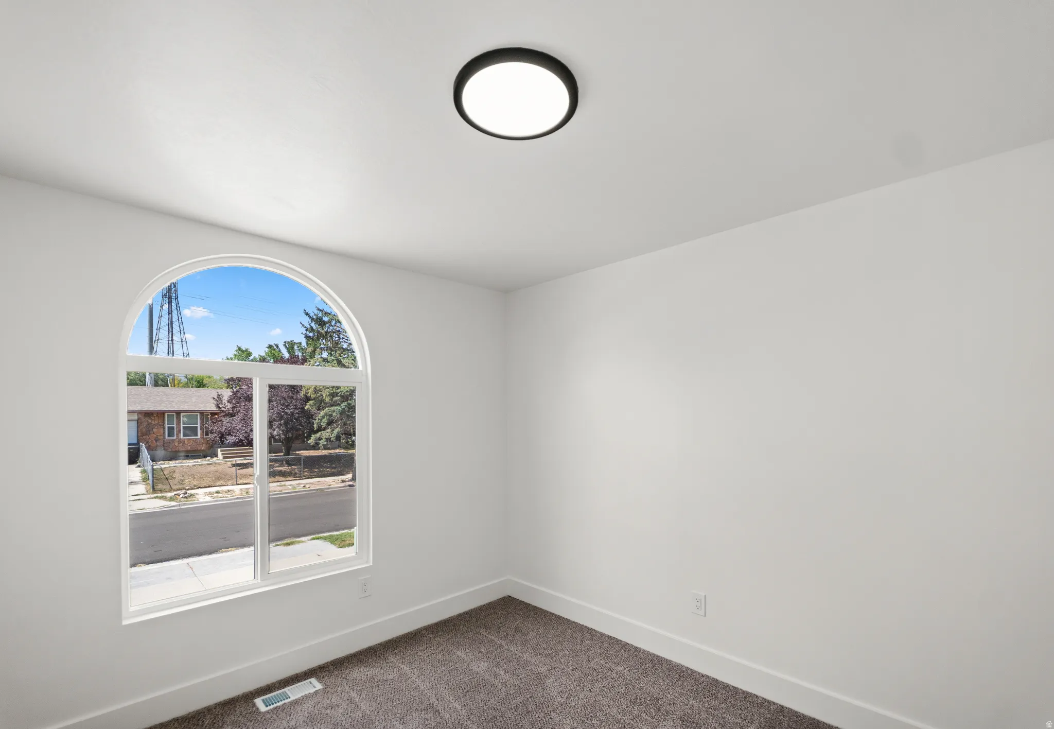 Arched window with street scenery, white walls, dark carpet flooring, and a flush-mount ceiling light fixture