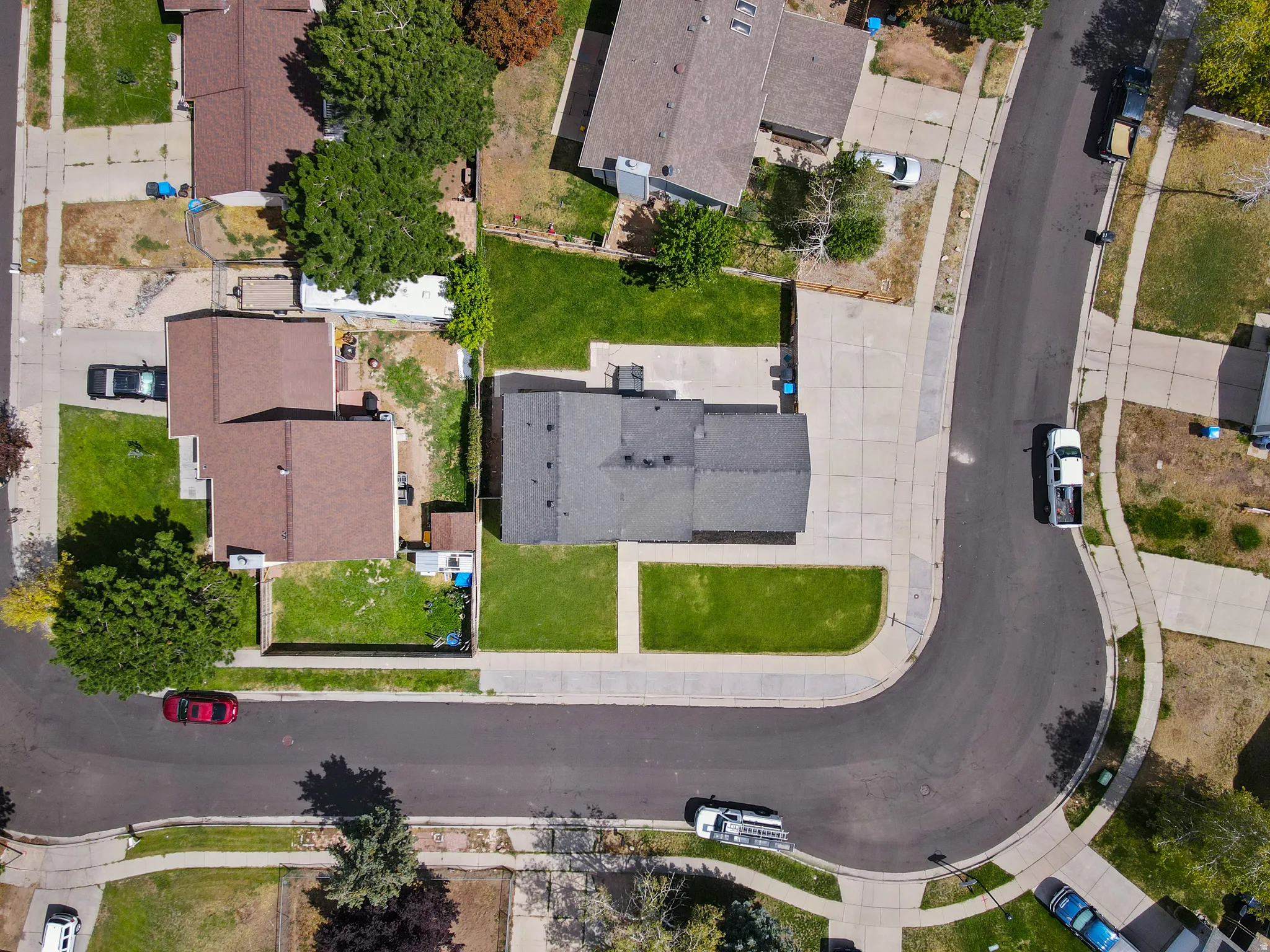 Corner lot residence with a dark roof, featuring a concrete driveway and an expansive front lawn