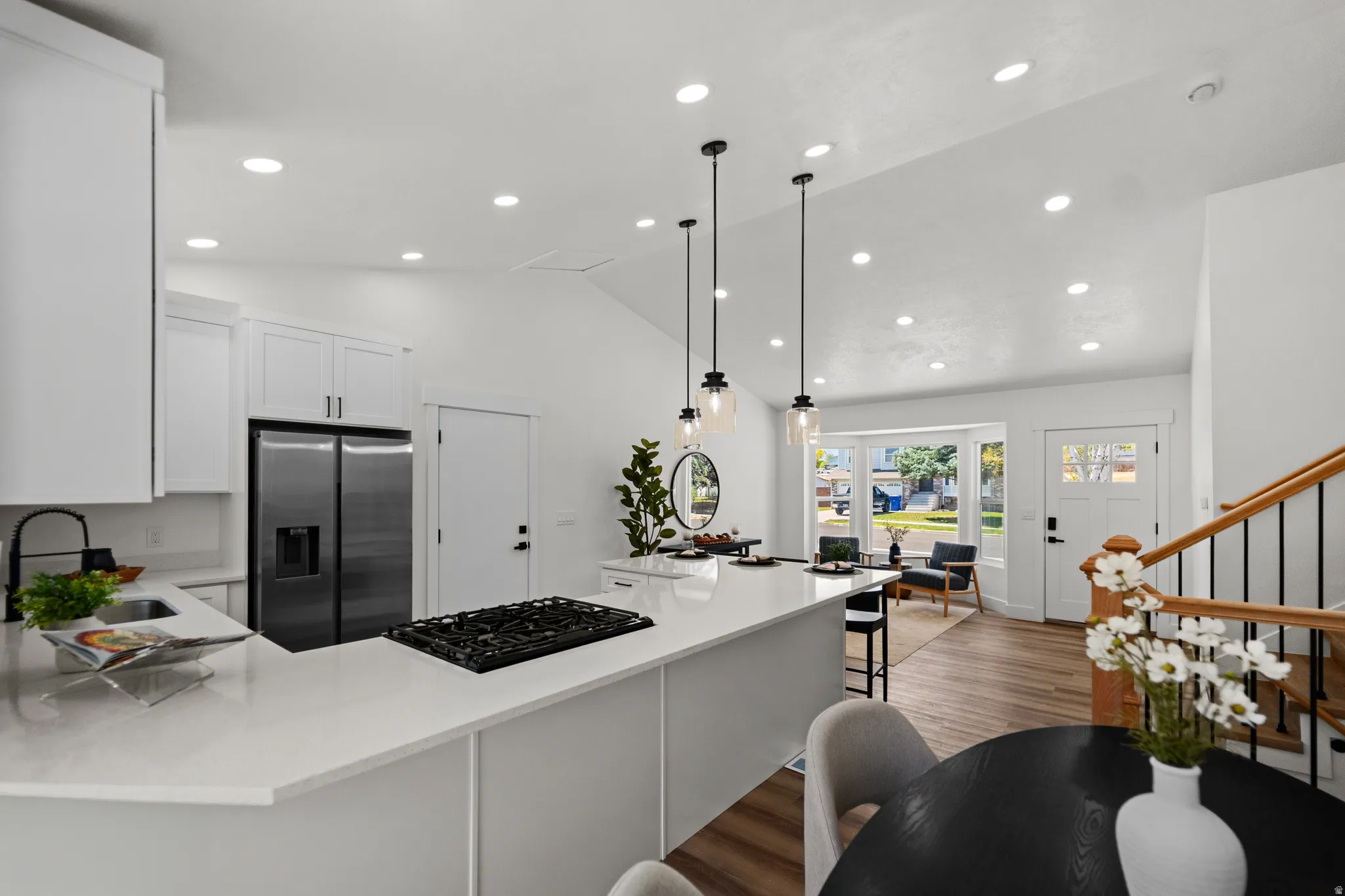 Open-concept living space with vaulted ceilings, recessed lighting, wood-finish flooring, a kitchen island with pendant lighting, and a bay window
