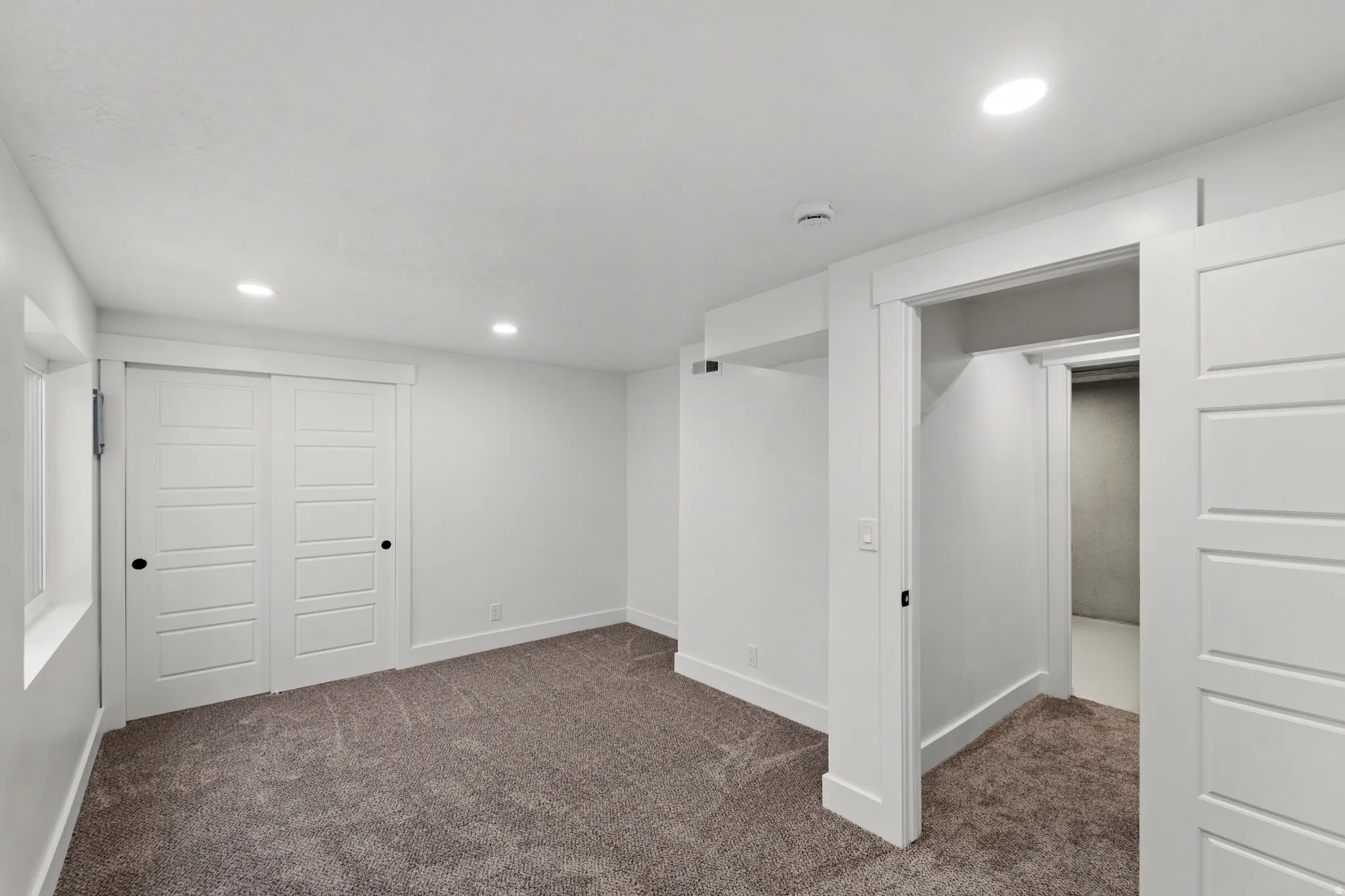 Recessed lighting, soft gray carpeting, white trim, white paneled doors, and a window