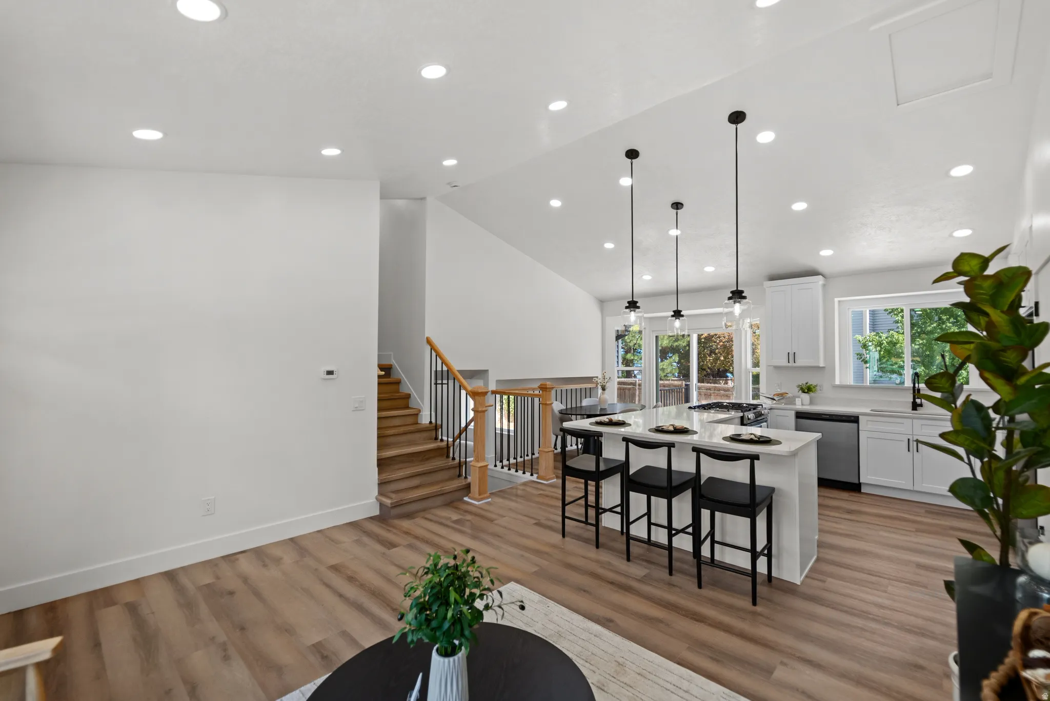 Vaulted ceiling with recessed lighting, wood-finish flooring, staircase with wood handrail and black balusters, kitchen island with seating, and white cabinetry