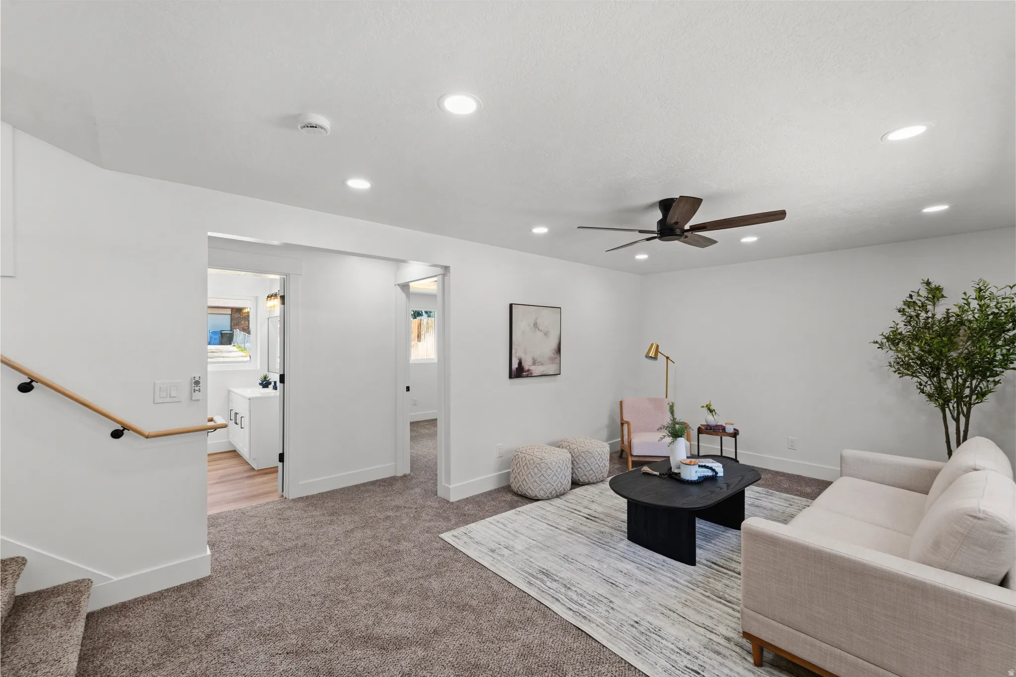 Recessed lighting, ceiling fan, wood-finish handrail with black mounts, plush carpeting, and white trim