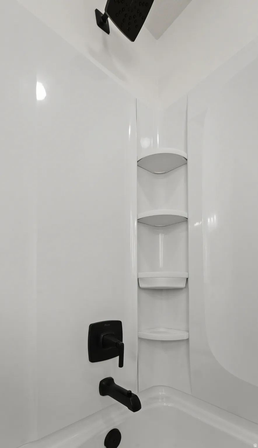 White acrylic shower surround with built-in corner shelving, matte black showerhead, and matching tub filler