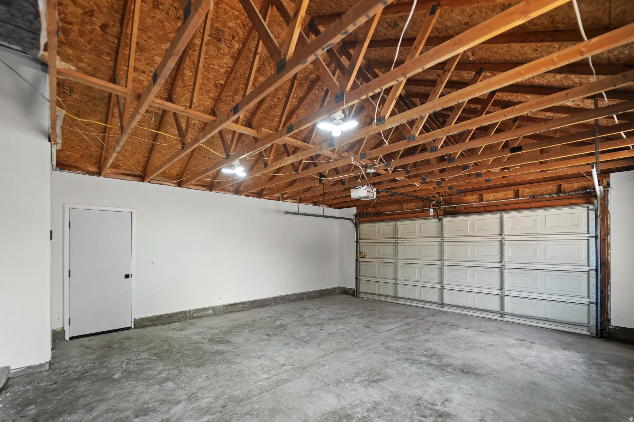 Concrete flooring, exposed wood ceiling joists, white paneled garage door, recessed lighting fixtures, and a white interior door