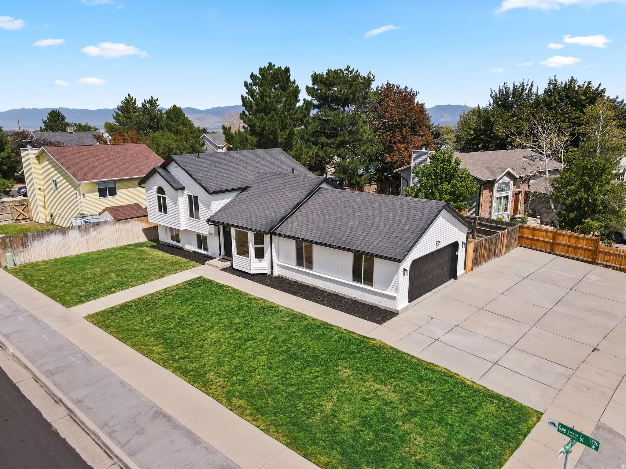 White exterior with dark trim accents, a dark asphalt shingle roof, a two-car garage, manicured front lawn, and an expansive concrete driveway