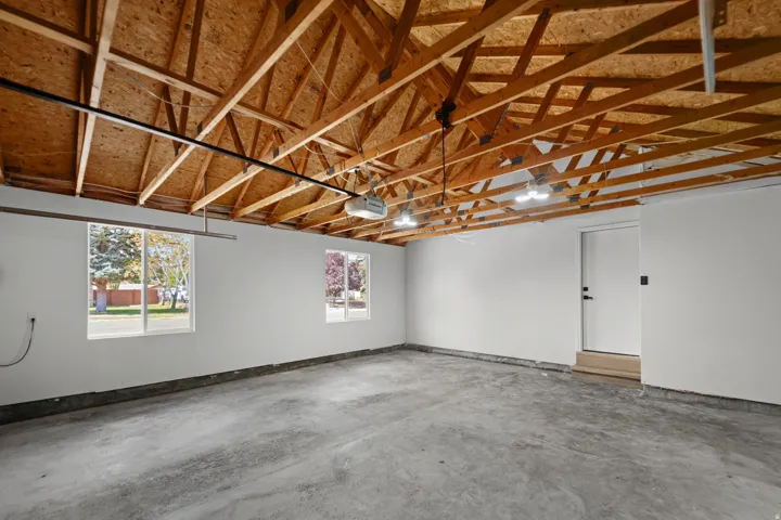 Exposed wood beam ceiling, concrete flooring, two large windows, white walls, and a white interior door