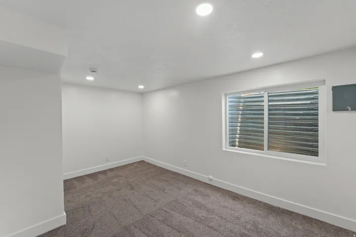 Recessed ceiling lighting, white painted walls, gray patterned carpet, white window frame, and white trim