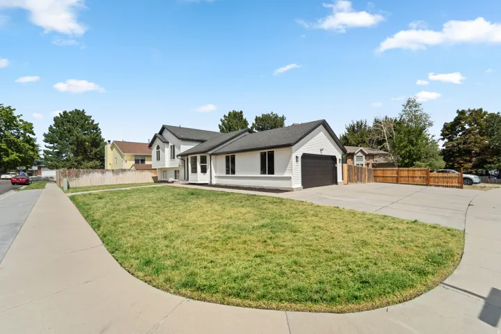White exterior siding with dark trim, attached garage with a dark door, concrete driveway, and front lawn