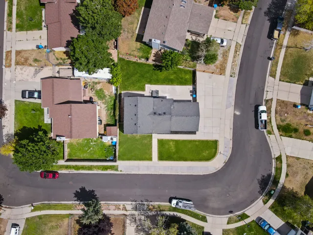 Corner lot residence with a dark roof, featuring a concrete driveway and an expansive front lawn