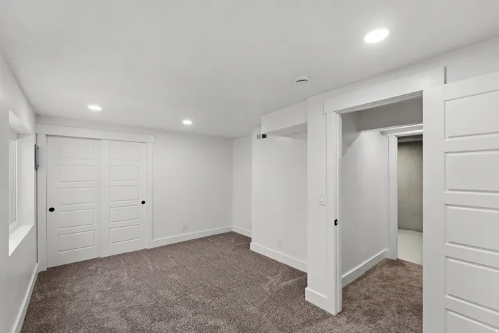 Recessed lighting, soft gray carpeting, white trim, white paneled doors, and a window