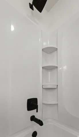 White acrylic shower surround with built-in corner shelving, matte black showerhead, and matching tub filler
