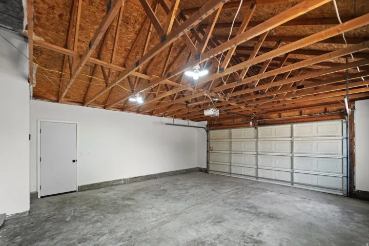 Concrete flooring, exposed wood ceiling joists, white paneled garage door, recessed lighting fixtures, and a white interior door