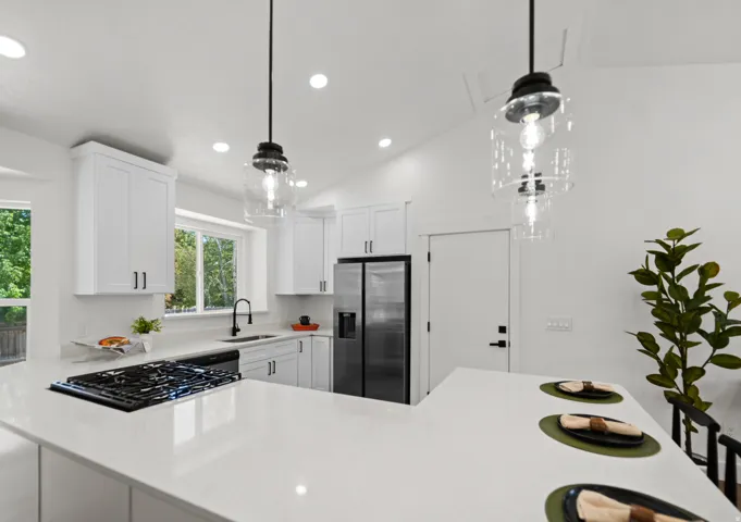 White shaker cabinetry, light-toned countertops, stainless steel refrigerator, black finish gas range, and a black finish gooseneck faucet