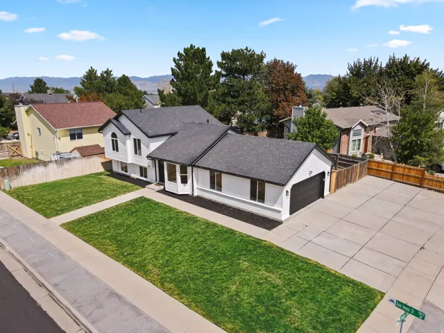 White exterior with dark trim accents, a dark asphalt shingle roof, a two-car garage, manicured front lawn, and an expansive concrete driveway