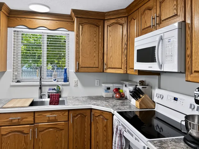 Kitchen featuring wood-finish cabinetry, built-in microwave, integrated sink, and white electric range