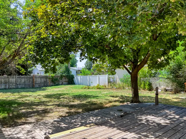 Expansive backyard featuring a wood deck, mature trees, and a combination of wood and vinyl fencing