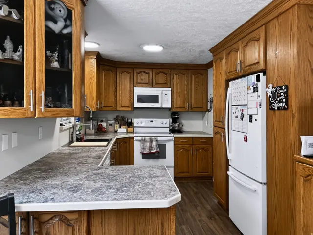 Warm wood cabinetry throughout this kitchen features glass-front upper cabinets, white appliances, and ample counter space with gray-toned countertops