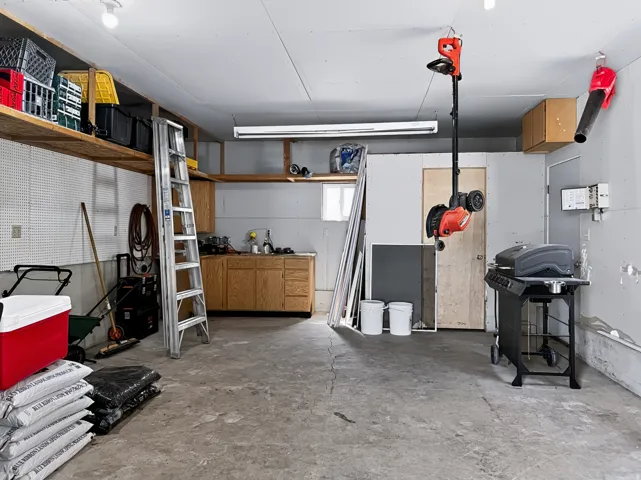 Garage with concrete flooring, fluorescent lighting, built-in wooden shelving, and a built-in wooden cabinet with a stainless steel sink