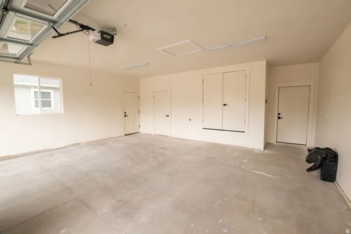 Spacious garage with a concrete floor, overhead garage door opener, multiple utility doors, and a window for natural light