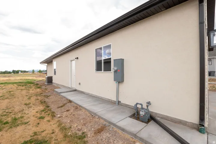 Stucco exterior with dark soffit and fascia, concrete walkway, and exterior lighting fixture