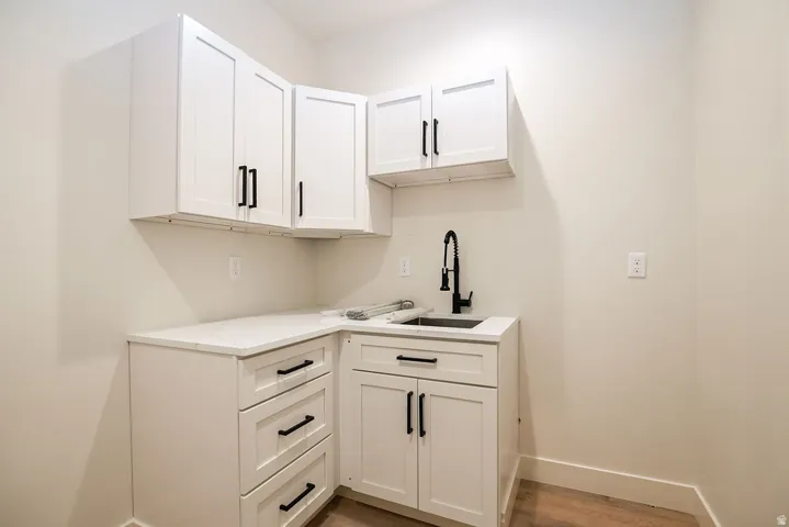 White shaker-style cabinetry, white countertops, black gooseneck faucet, stainless steel sink, wood-finish flooring