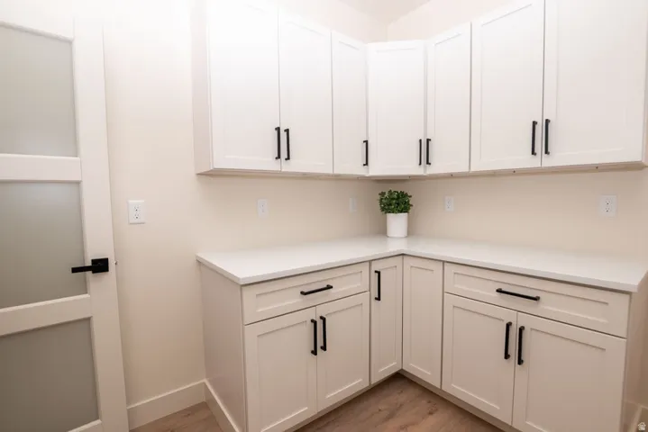 White shaker-style cabinetry with black hardware, white countertops, and wood-finish flooring