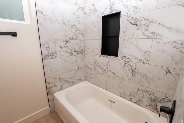 White bathtub with black bath fixtures, a recessed black shelf, and white-veined wall tiling