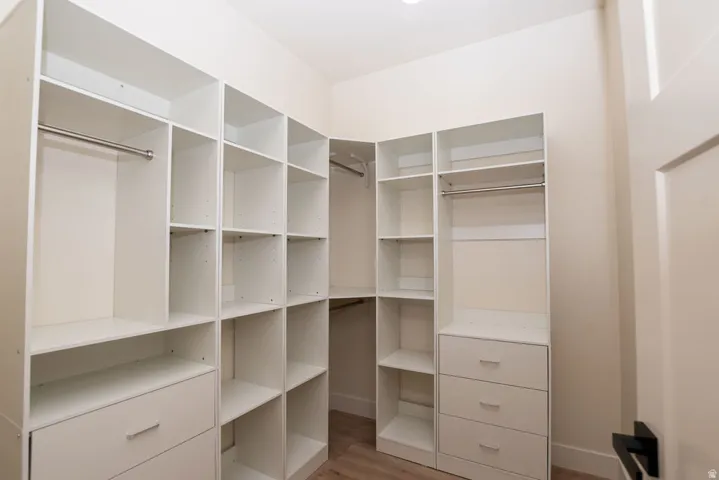 Walk-in closet featuring built-in white shelving, integrated drawers with metal pulls, and chrome hanging rods