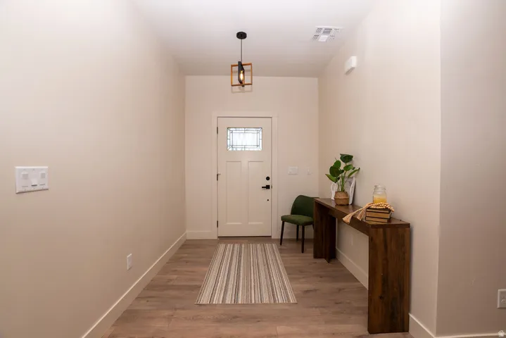 Entryway featuring wood-finish flooring, a contemporary pendant light fixture, and a solid entry door with decorative glass