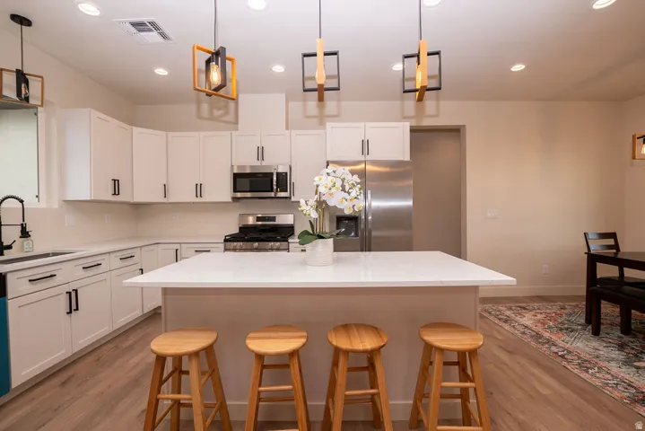 Kitchen featuring white cabinetry, stainless steel appliances, a center island with a white countertop, and wood-finish flooring